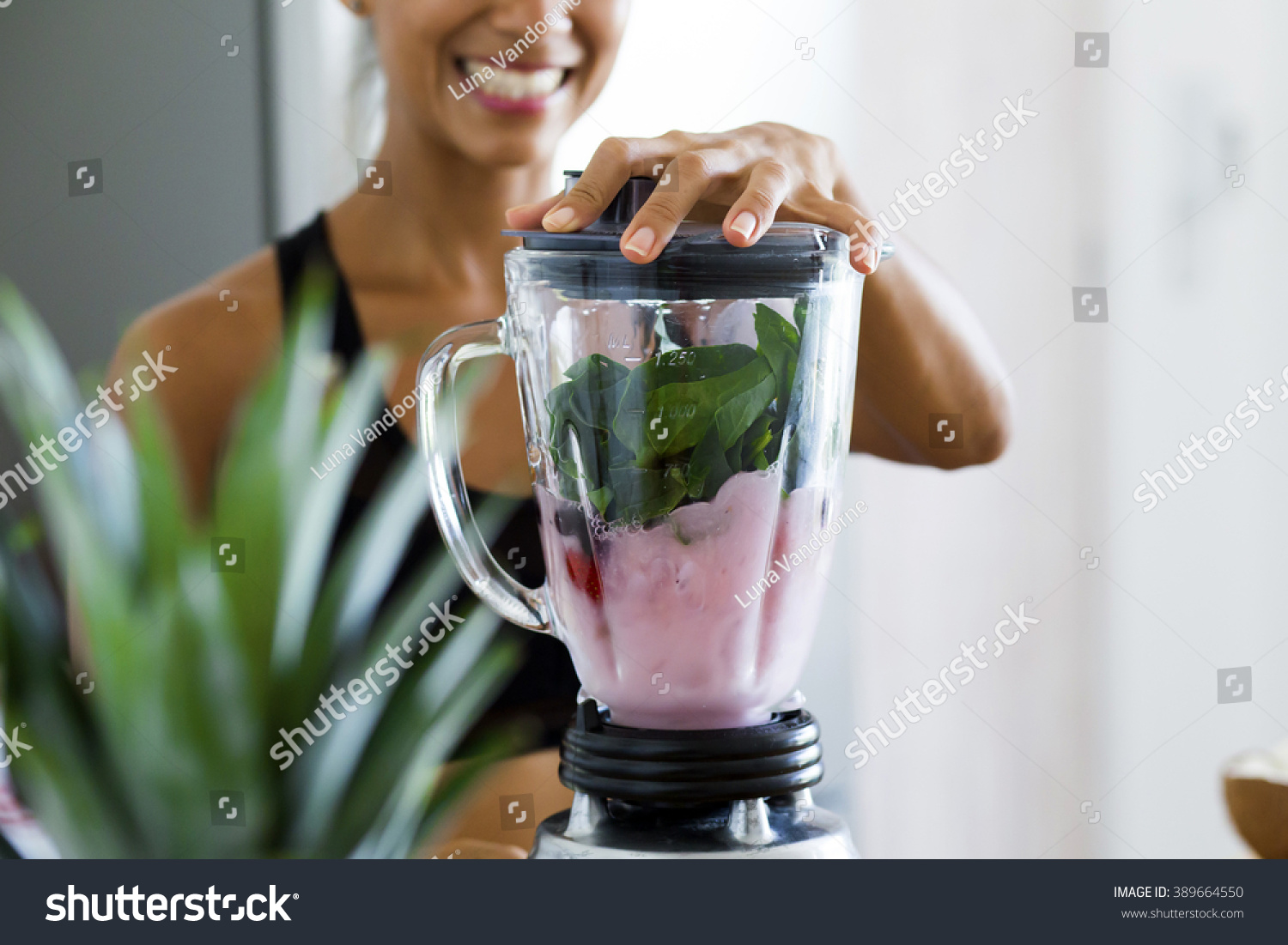 Woman blending spinach, berries, bananas and almond milk to make a healthy green smoothie #389664550
