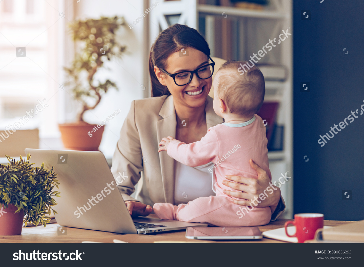 Working together is so fun! Cheerful young beautiful businesswoman looking at her baby girl with smile while sitting at her working place #390656293