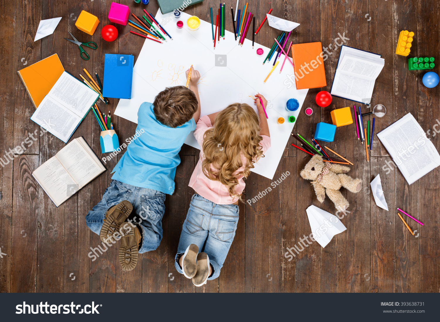 Happy children. Top view creative photo of little boy and girl on vintage brown wooden floor. Children lying near books and toys, and painting #393638731