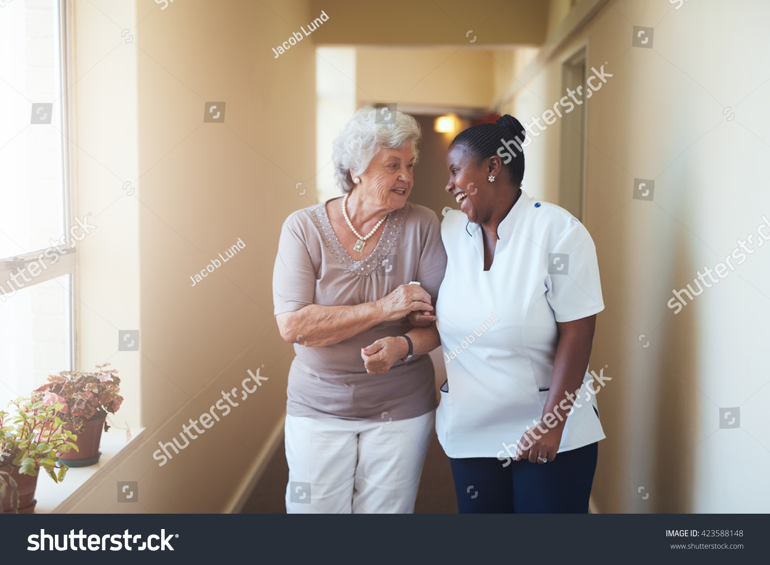 Portrait of happy female caregiver and senior woman walking together at home. Professional caregiver taking care of elderly woman. #423588148