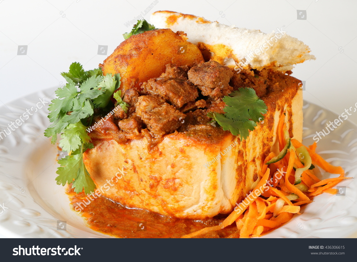 Closeup of lamb "bunny chow" - the popular, Indian fast food cuisine which originated in South Africa, with carrot salad  #436306615