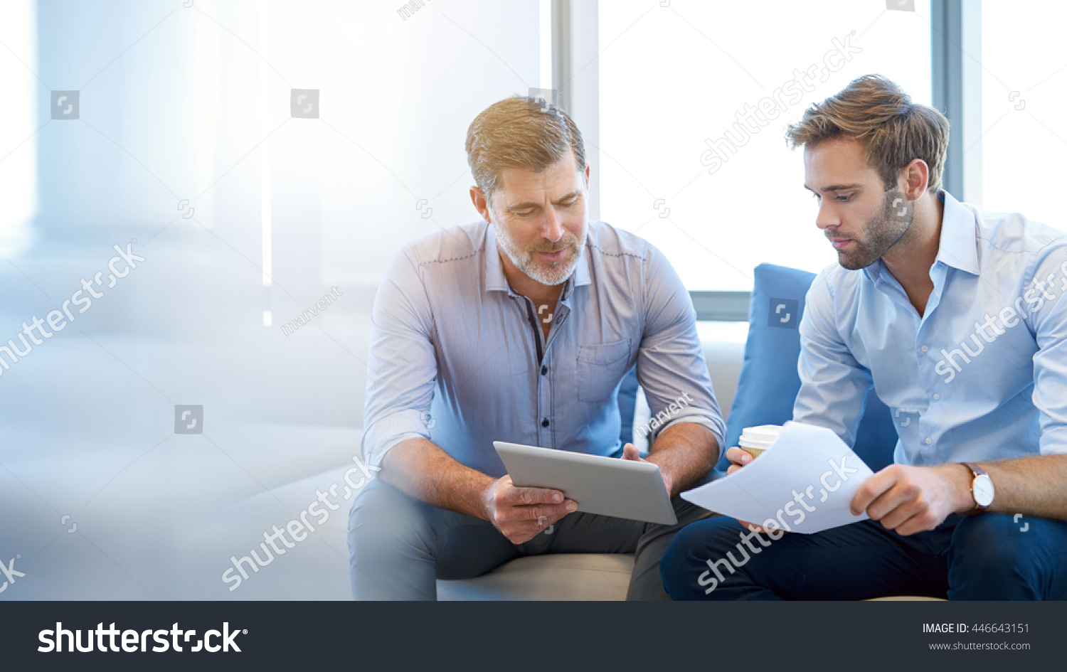 Mature businessman using a digital tablet to discuss information with a younger colleague in a modern business lounge #446643151