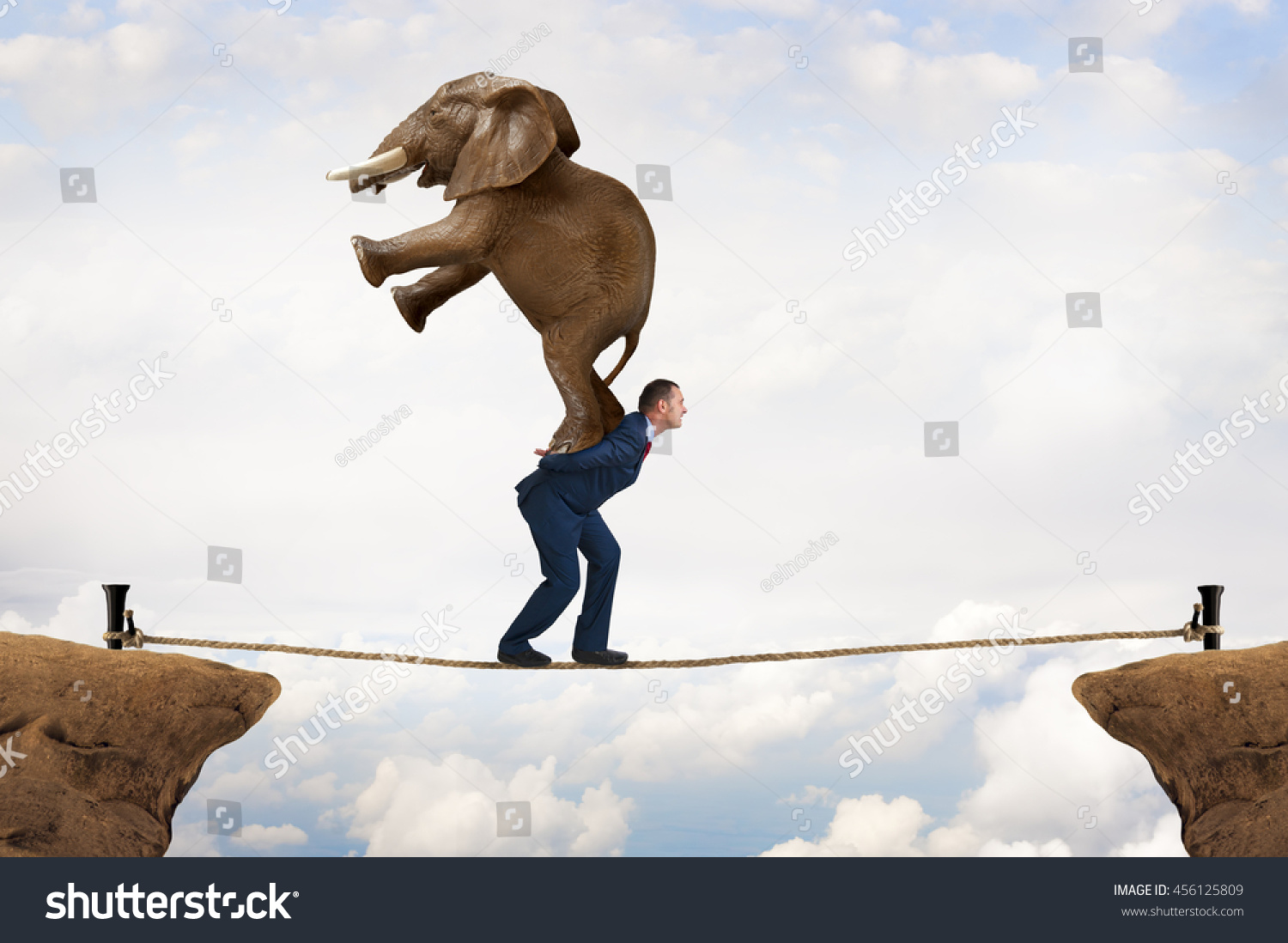 business challenge concept businessman carrying an elephant across a tightrope chasm #456125809
