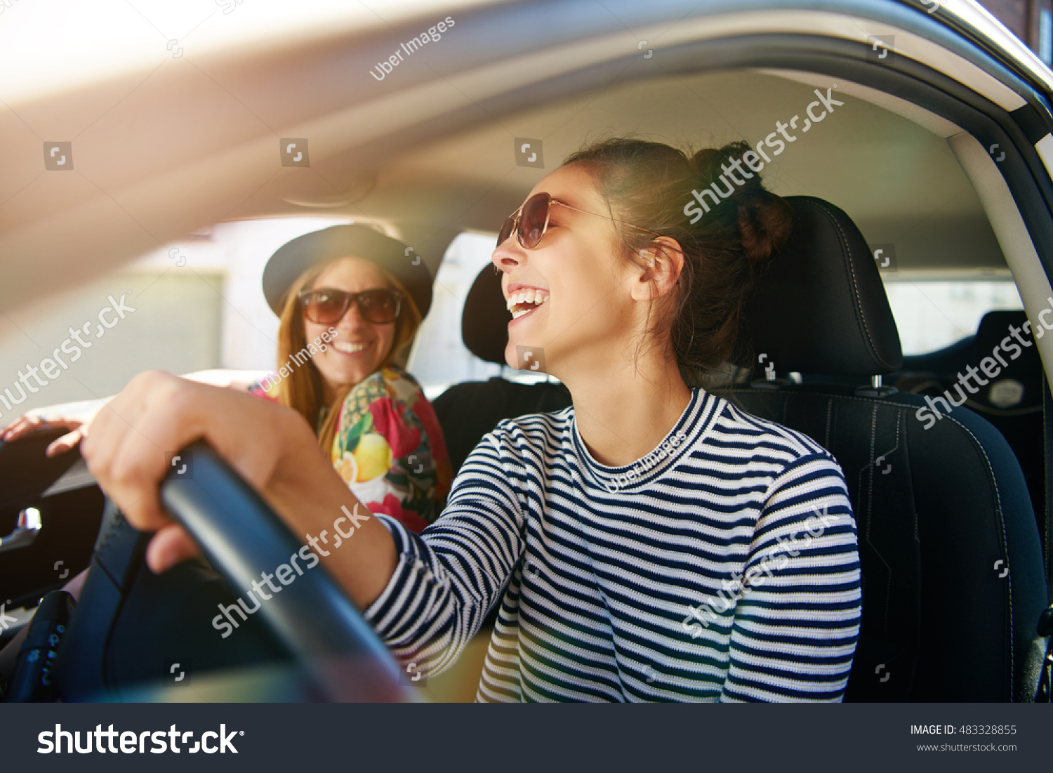Smiling happy young woman giving her friend a lift in her car in town, profile view through the open side window with sun flare #483328855