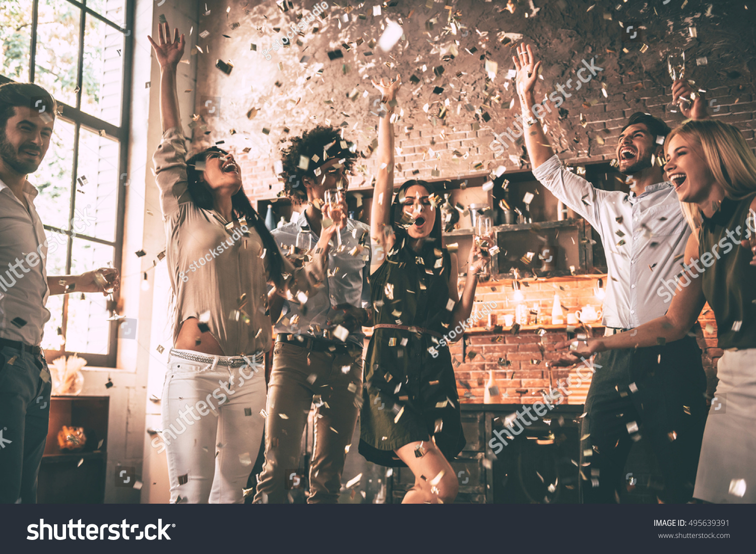 Confetti fun. Group of happy young people throwing confetti and jumping while enjoying home party on the kitchen  #495639391
