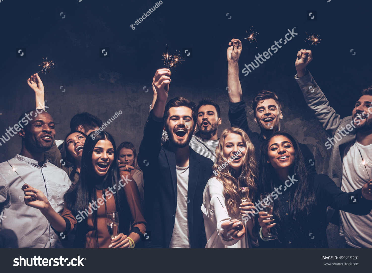 Party with friends. Group of cheerful young people carrying sparklers and champagne flutes #499219201