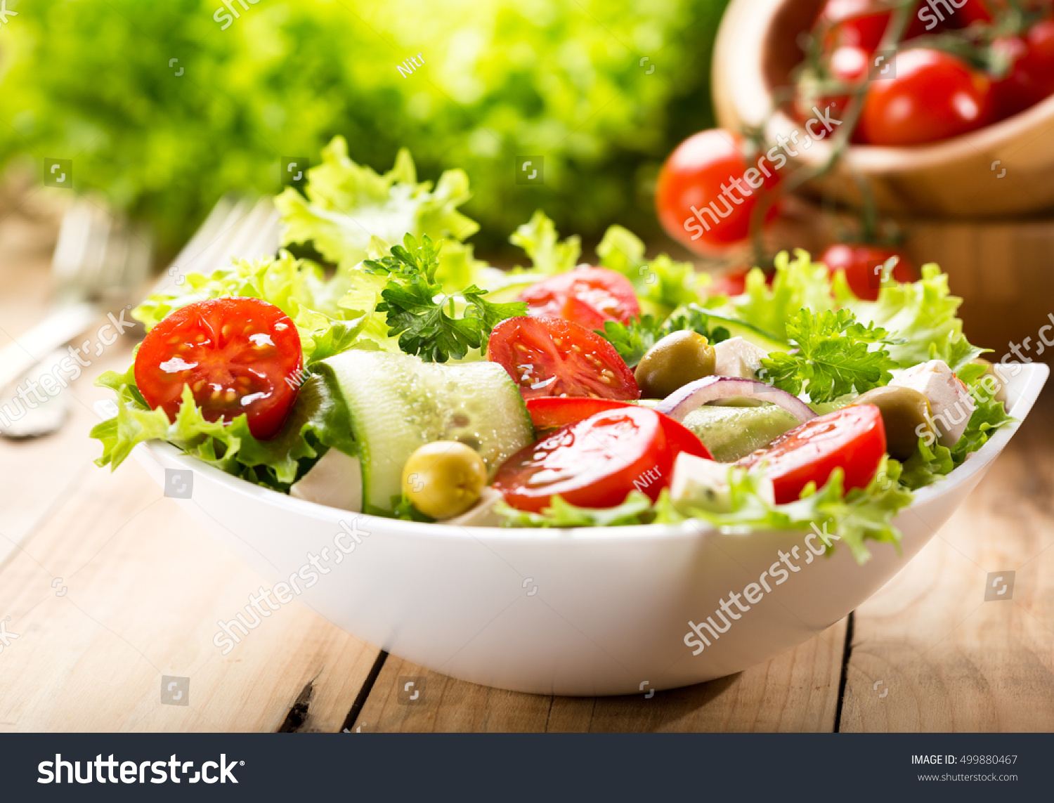 bowl of salad with vegetables and greens on wooden table #499880467
