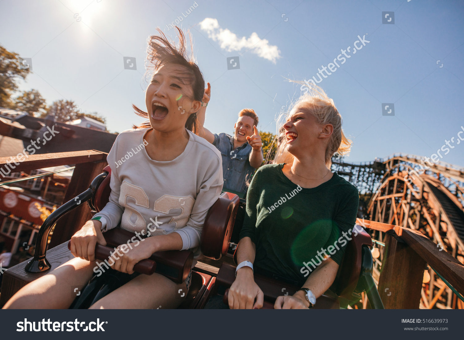 Young friends on thrilling roller coaster ride. Young women and men having fun at amusement park. #516639973