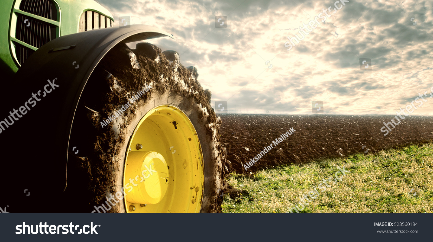 Agriculture. Tractor plowing field. Wheels covered in mud, field in the backround. Cultivated field. Agronomy, farming, husbandry concept. #523560184