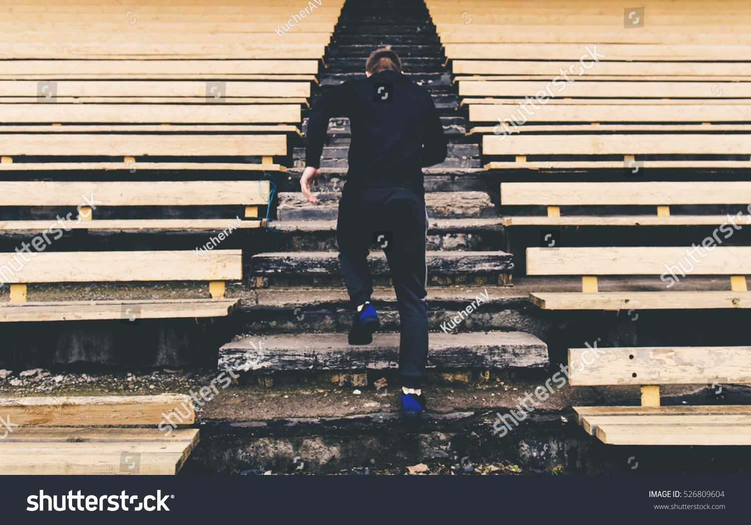 Young man runner in sport clothes running climbing stairs in the stadium #526809604