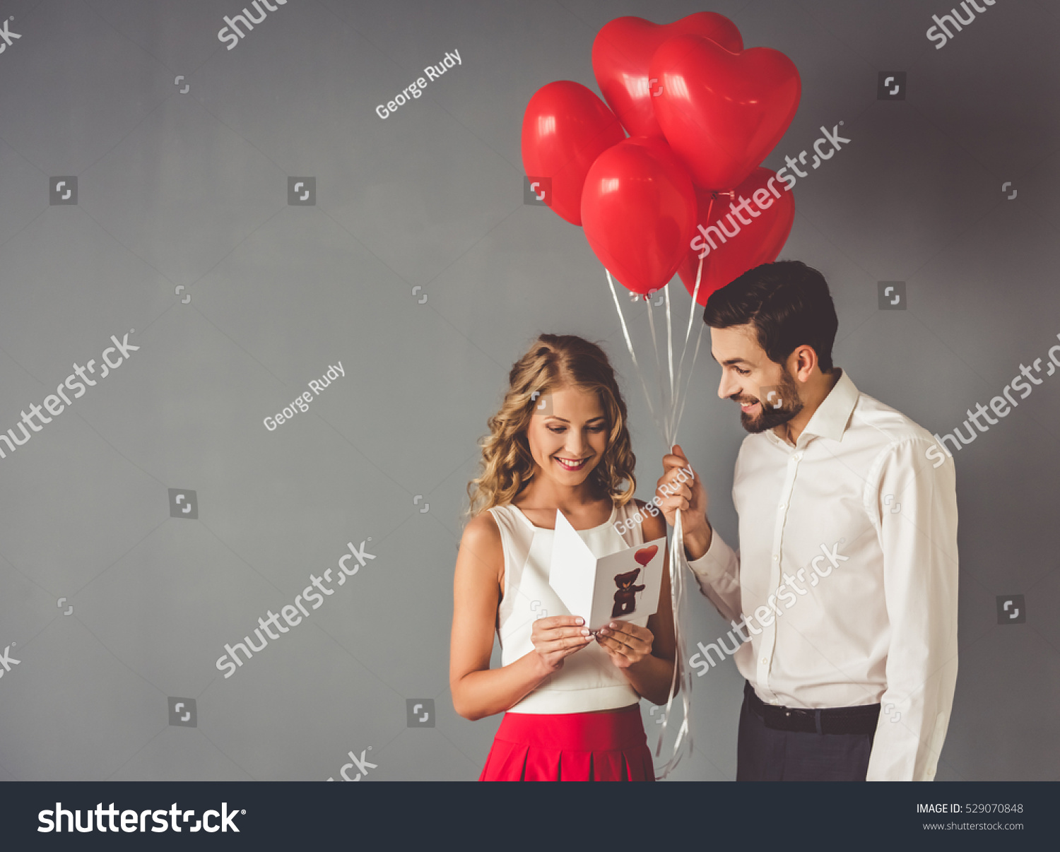 Handsome elegant guy is presenting a gift card and balloons to his beautiful girlfriend and smiling #529070848