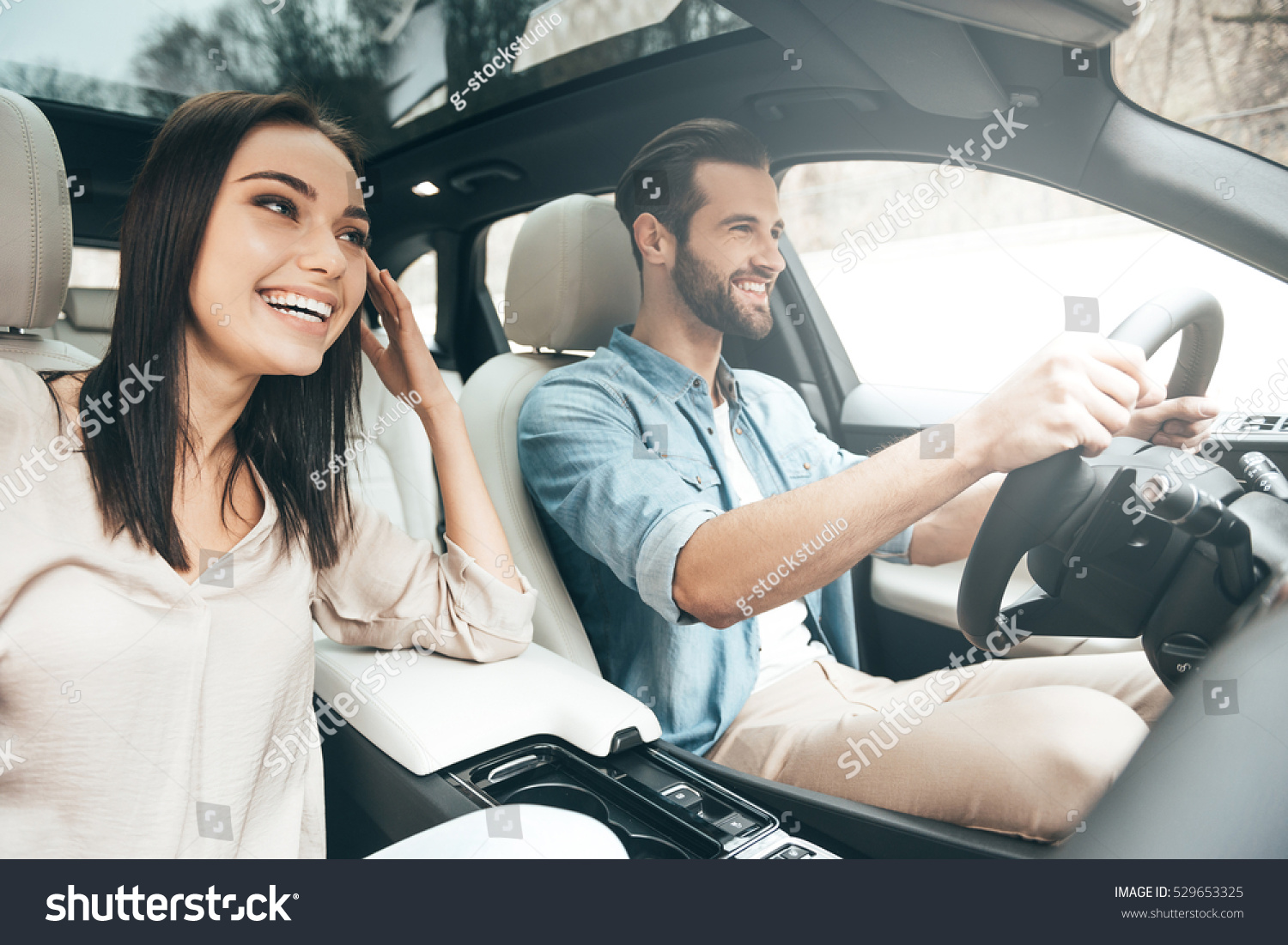 Enjoying travel. Beautiful young couple sitting on the front passenger seats and smiling while handsome man driving a car #529653325