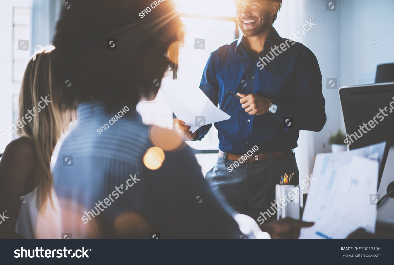 Hispanic businessman holding papers hands and smiling.Young team of coworkers making great business discussion in modern coworking office.Teamwork people concept.Horizontal, blurred background, flares #530013196
