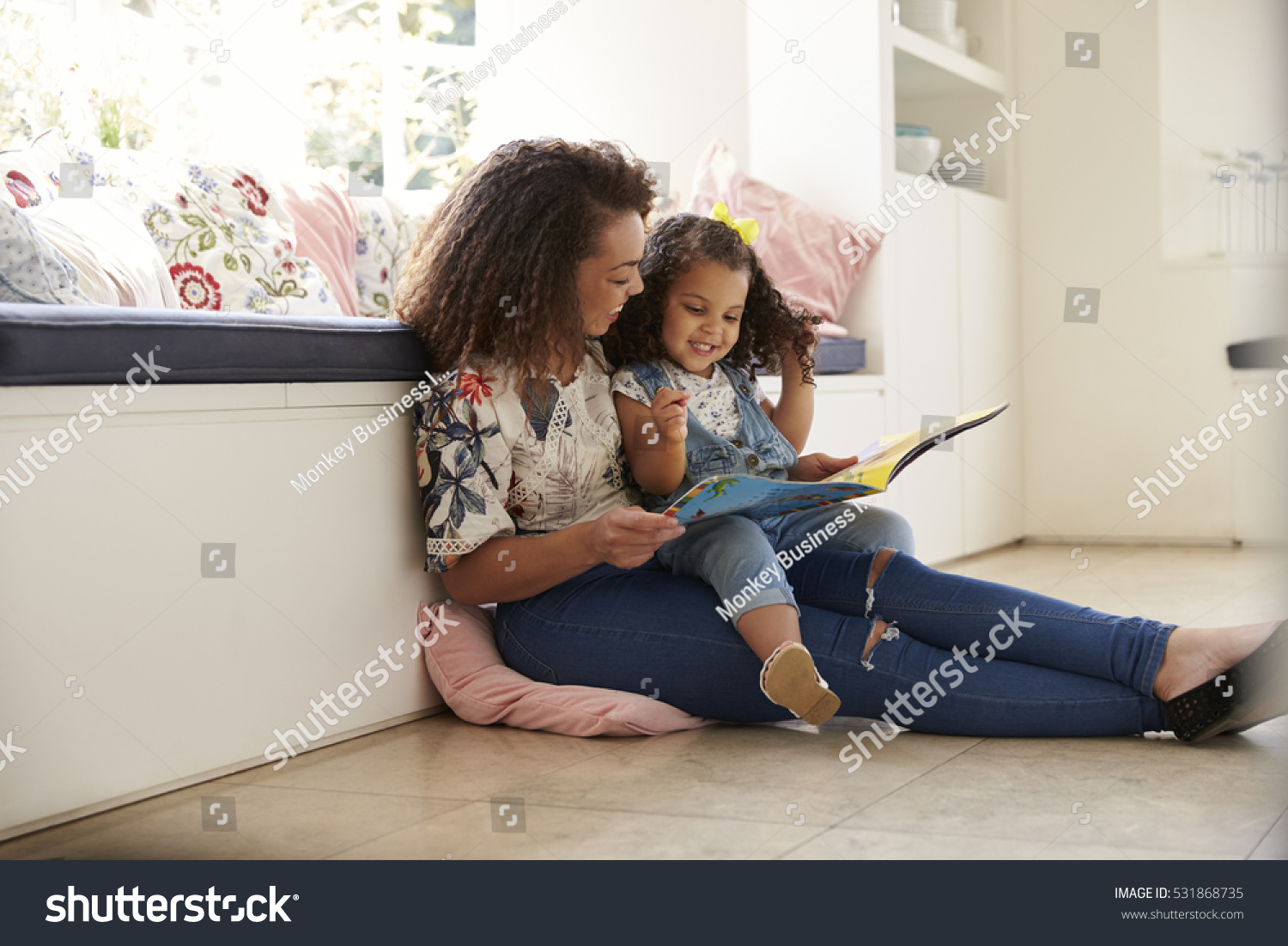 Mother sitting on the floor reading a book with her daughter #531868735
