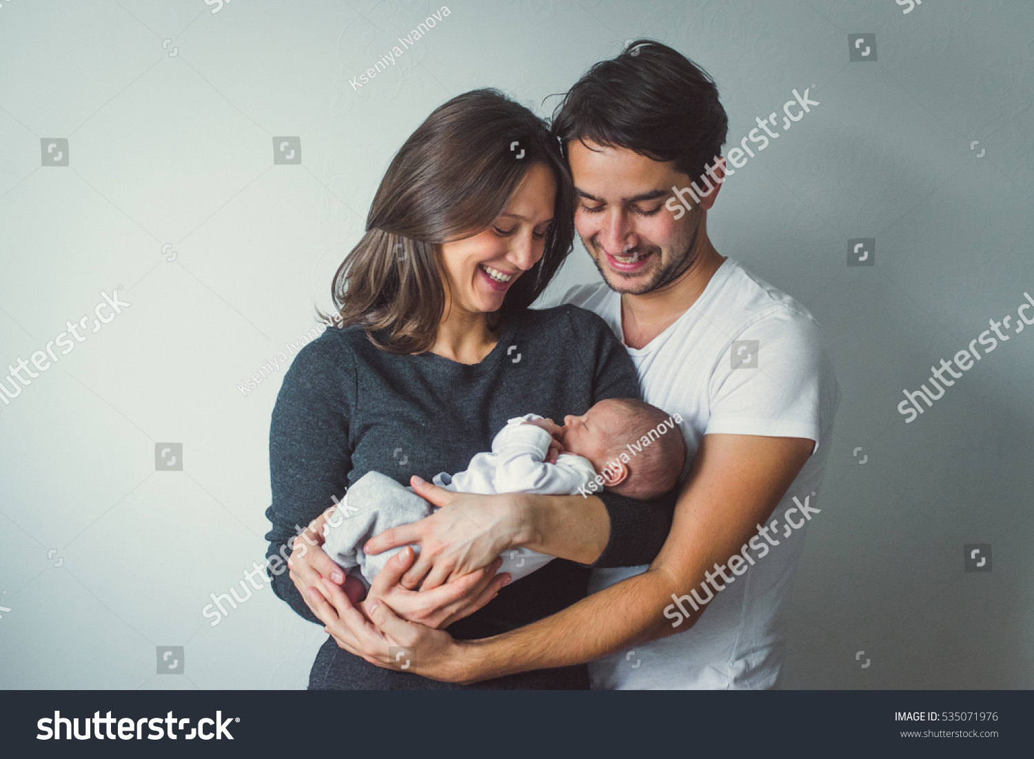 Woman and man holding a newborn. Mom, dad and baby. Close-up. Portrait of young smiling family with newborn on the hands. Happy family on a background.  #535071976