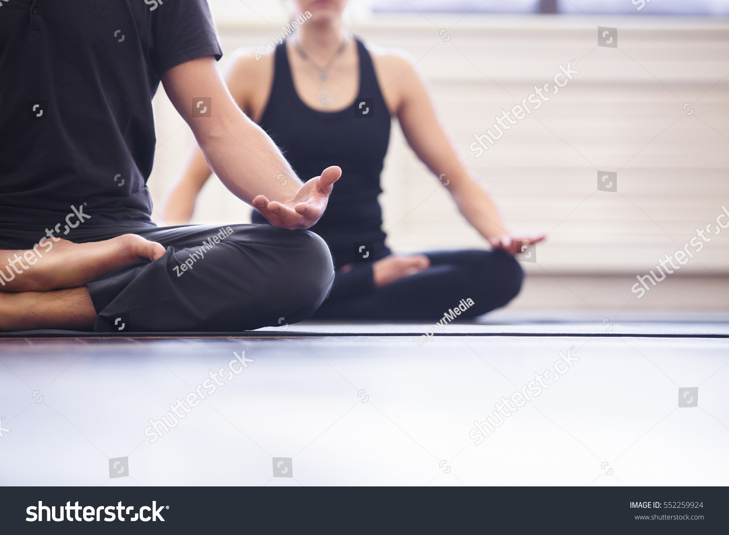 Yoga group concept. Young couple meditating together, sitting back to back on windows background, copy space #552259924
