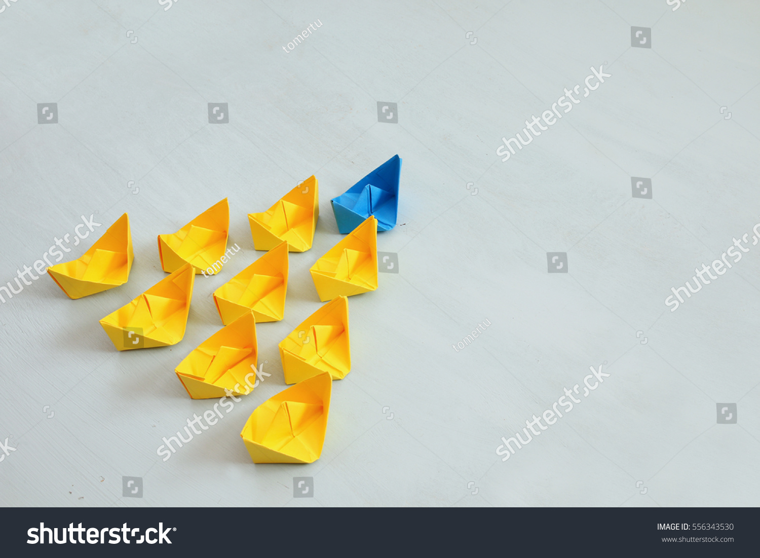 Leadership concept with paper boats on blue wooden background. One leader ship leads other ships. Filtered and toned image #556343530