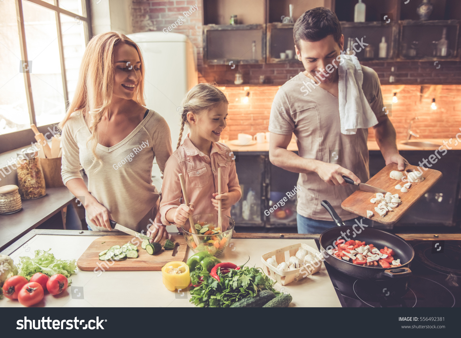 Cute little girl and her beautiful parents are  smiling while cooking in kitchen at home #556492381