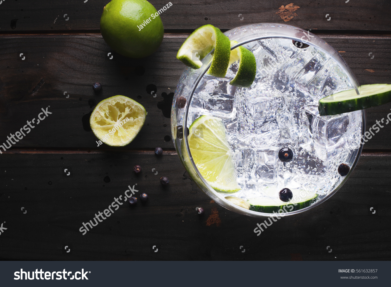 Glass of gin tonic with cucumber, lime and ice over a wooden table #561632857