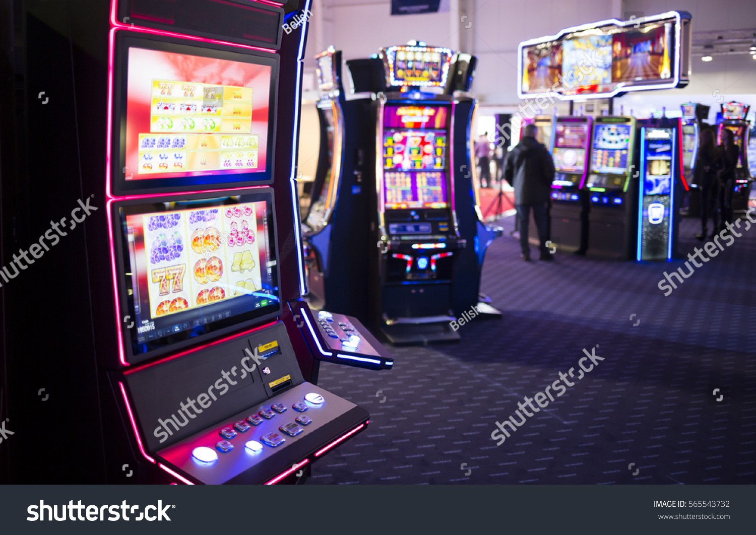 A slot machine is seen in a casino room with people playing other slot machines in the background. #565543732