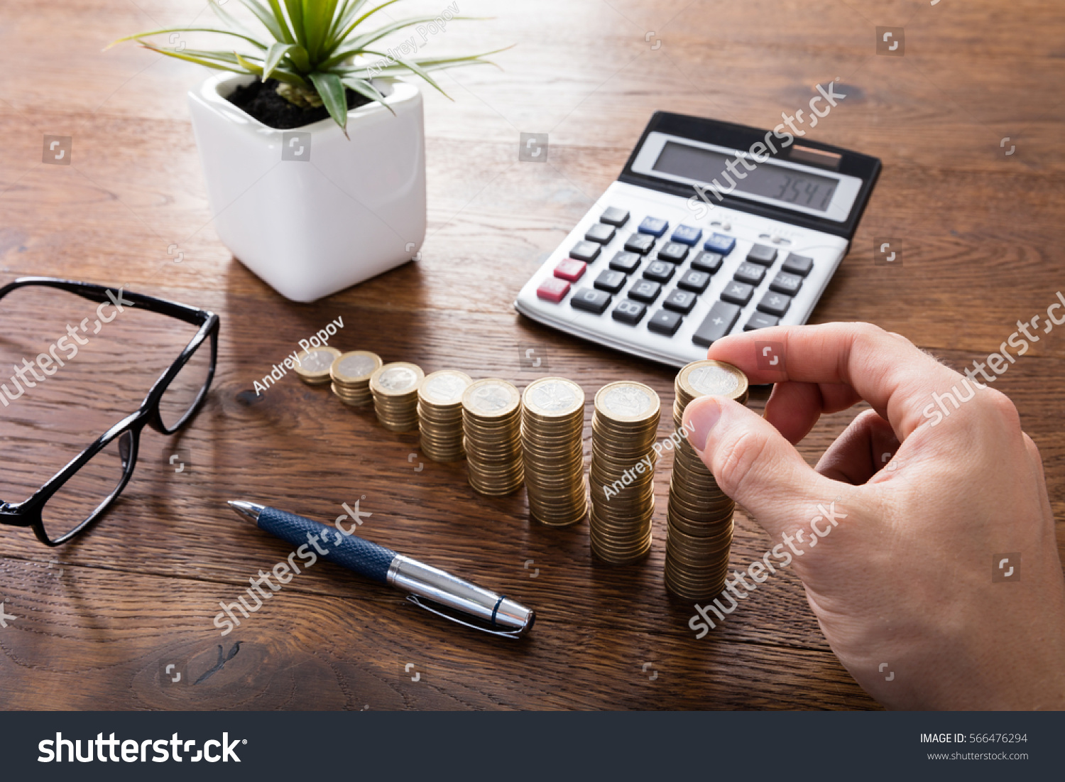 Close-up Of A Person Hand Calculating On Wooden Desk In Front Of Stacked Coins. Income Tax Raise Concept #566476294