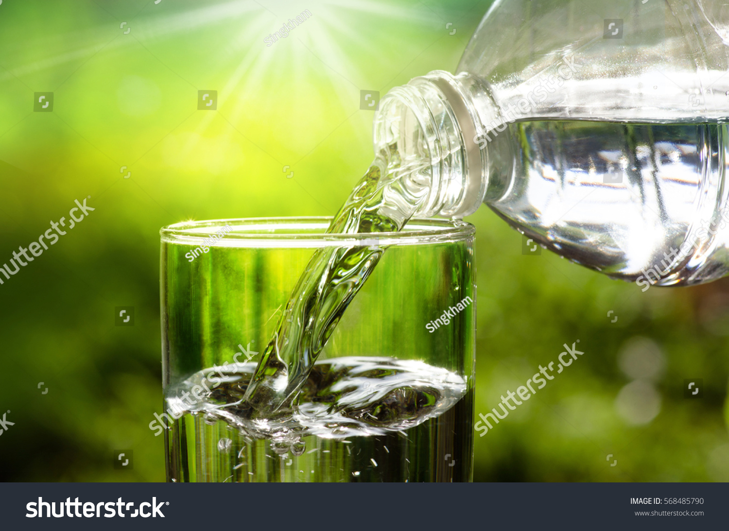 Pít vodu nalil do skla přes sluneční světlo a přírodní zelené pozadí #568485790