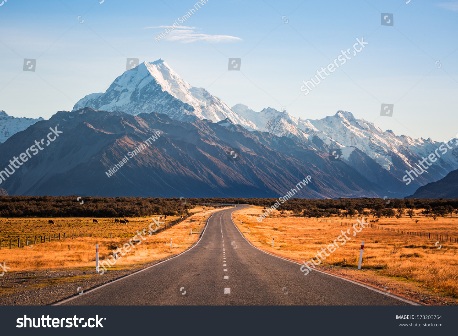 A long road leading to a large snow capped mountain on a sunny day #573203764