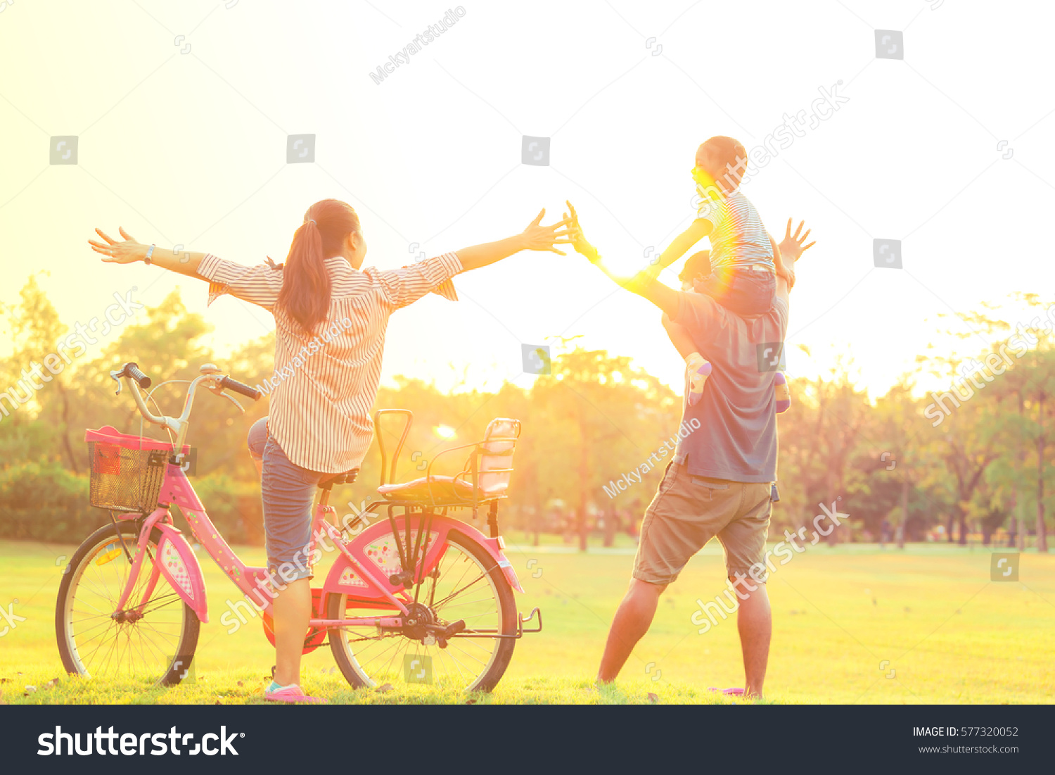 Silhouette of happy little girl child running into arms of his loving mother for hug with sun flare, in front sunset in the sky on Chatuchak Park at Bangkok City, Thailand. Concept of friendly family. #577320052