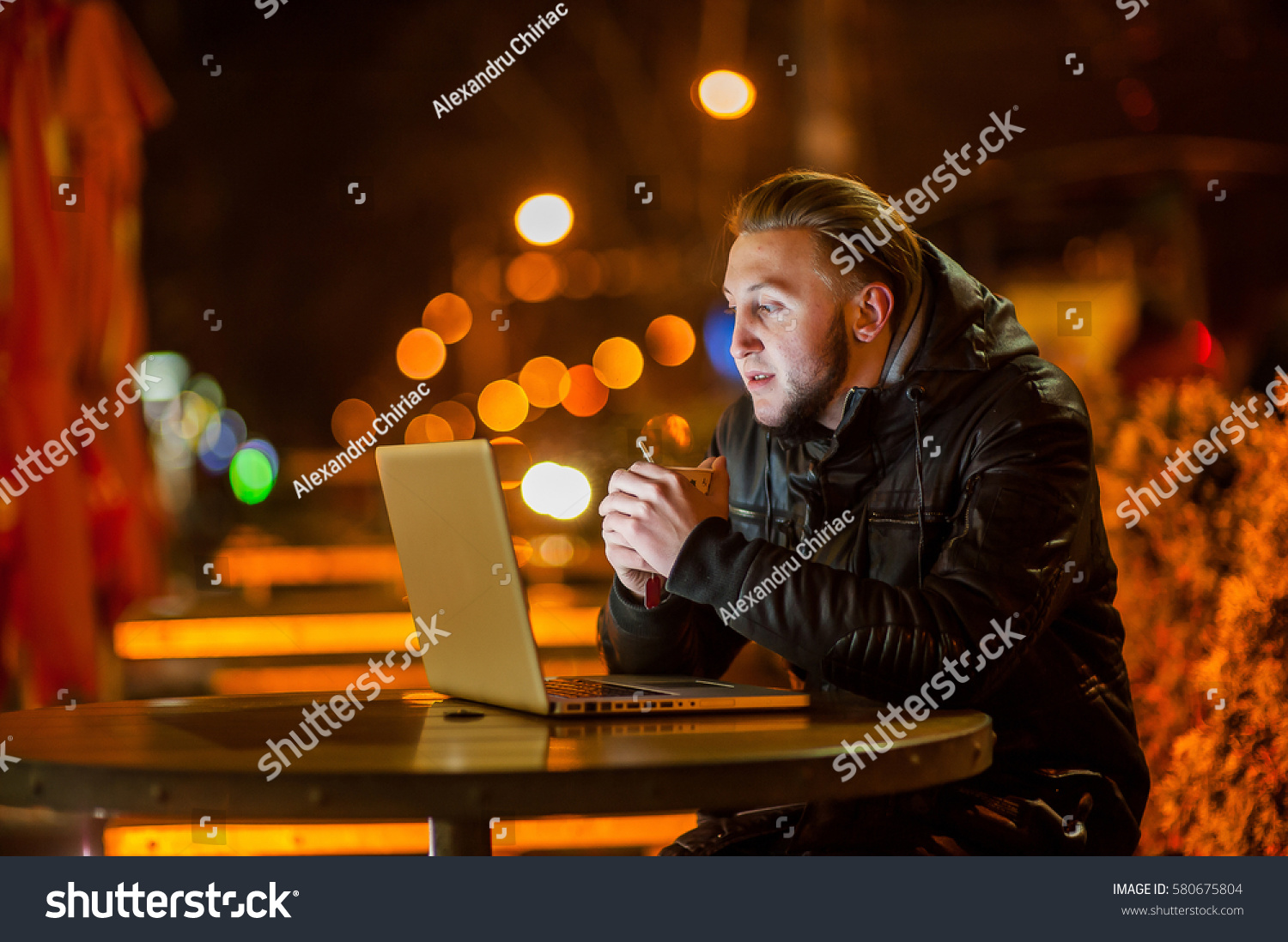 handsome young man with a computer on the street at night #580675804