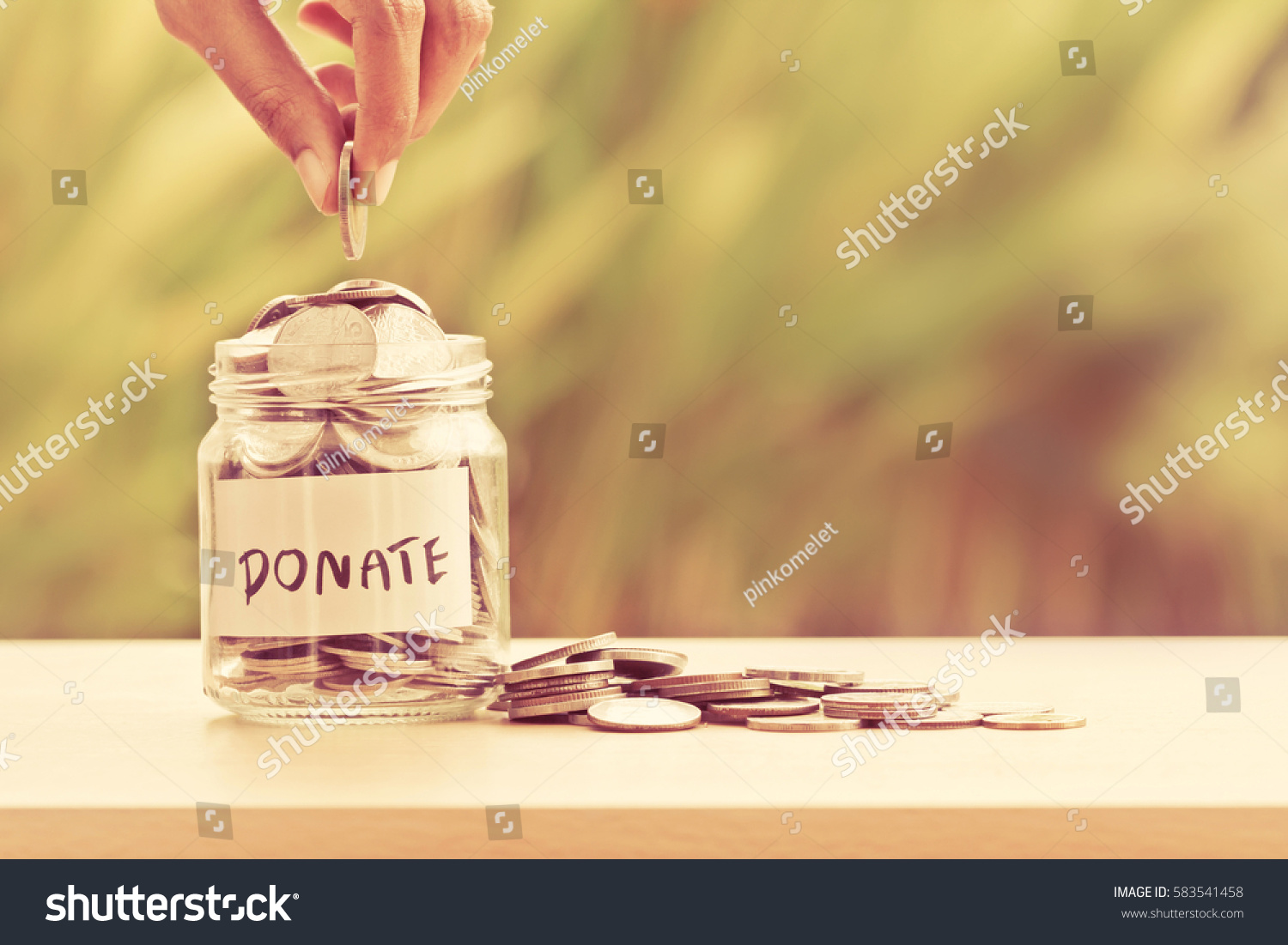 Hand putting Coins in glass jar with DONATE word written text label for giving and donation concept #583541458
