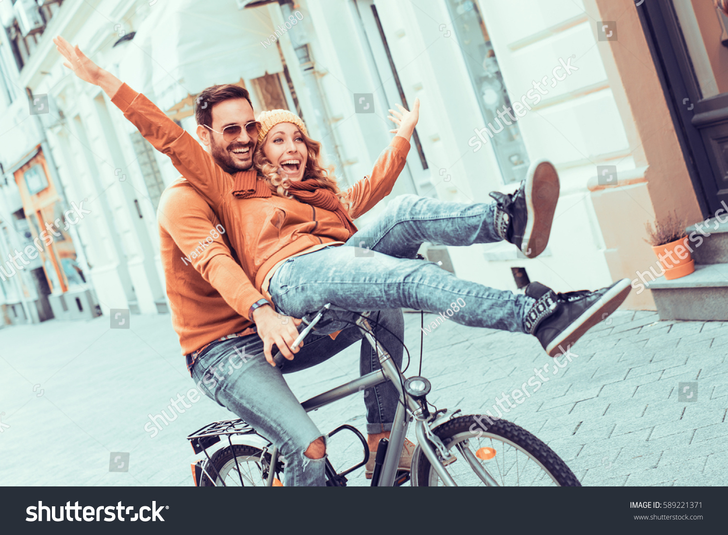 Young couple having fun in the city.Happy young couple going for a bike ride on a autumn day in the city. #589221371