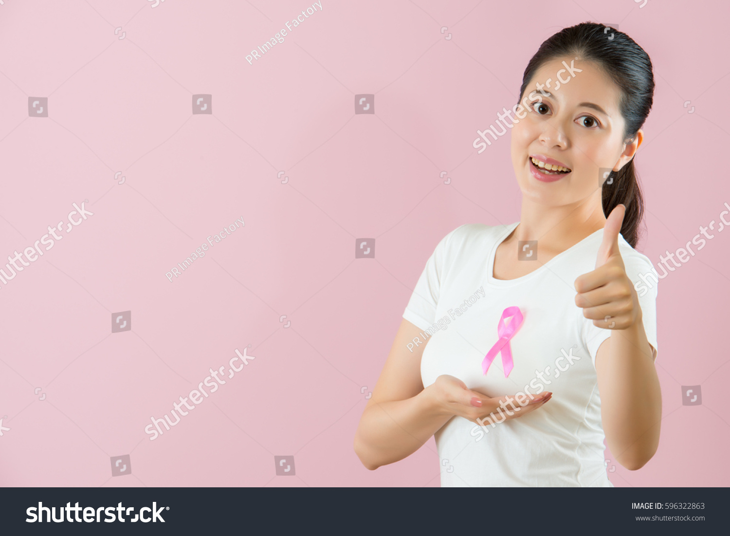medical and health concept. healthy Chinese Asian model smile showing thumb up and hand under breast expressing fighting against cancer successful isolated on pink background. #596322863