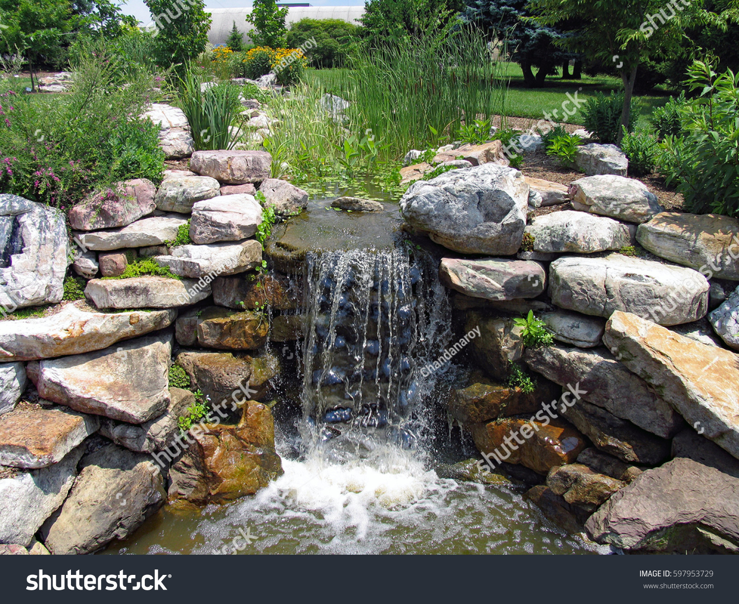 A lush green garden with waterfall cascading down the rocky stones #597953729