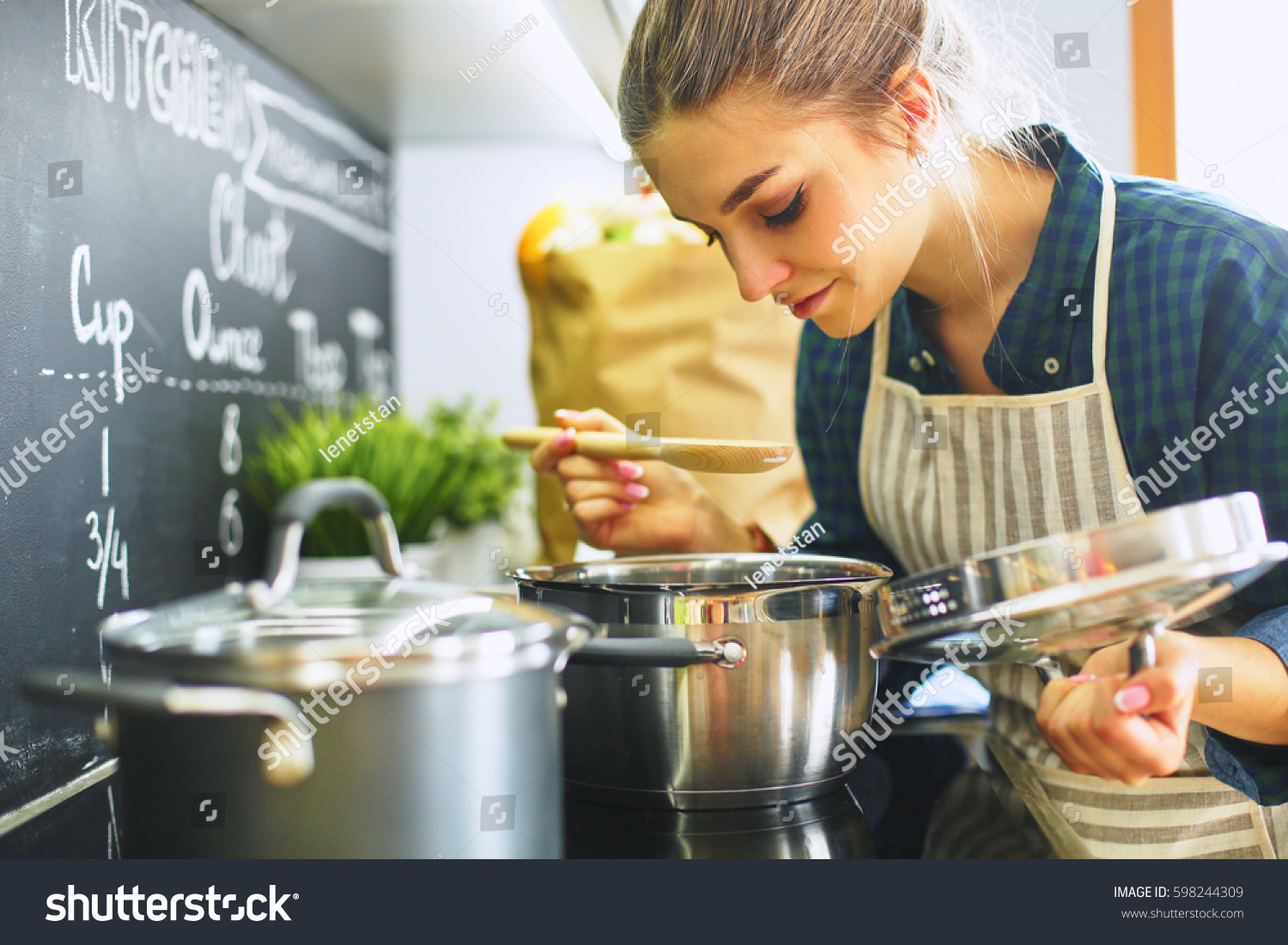 Young woman cooking in her kitchen standing near stove #598244309