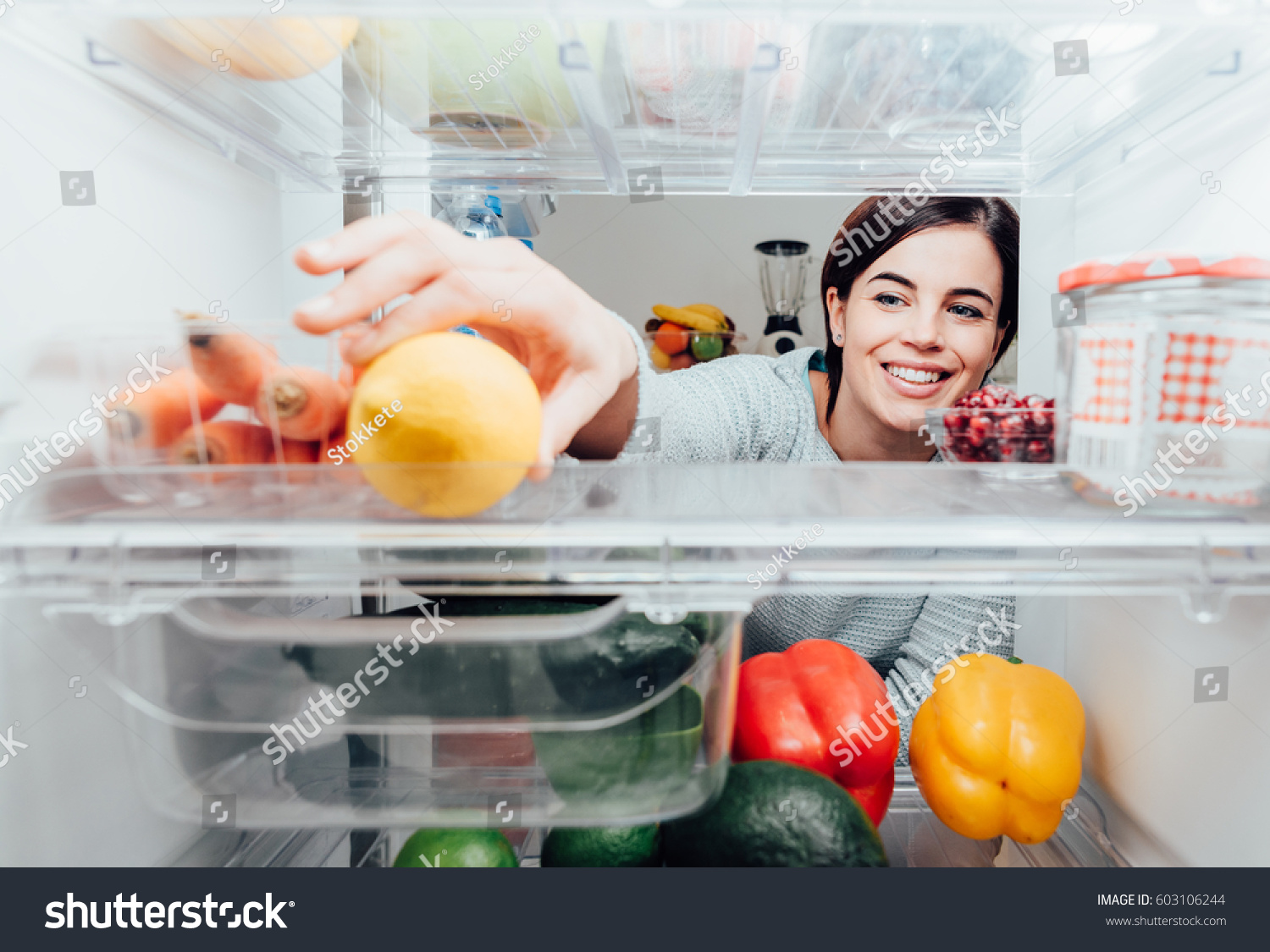 Smiling woman taking a fresh lemon out of the fridge, healthy food concept #603106244