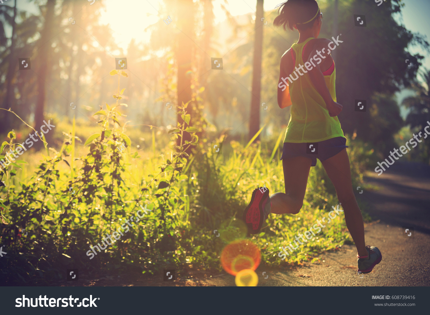 Young fitness woman running at morning tropical forest trail  #608739416