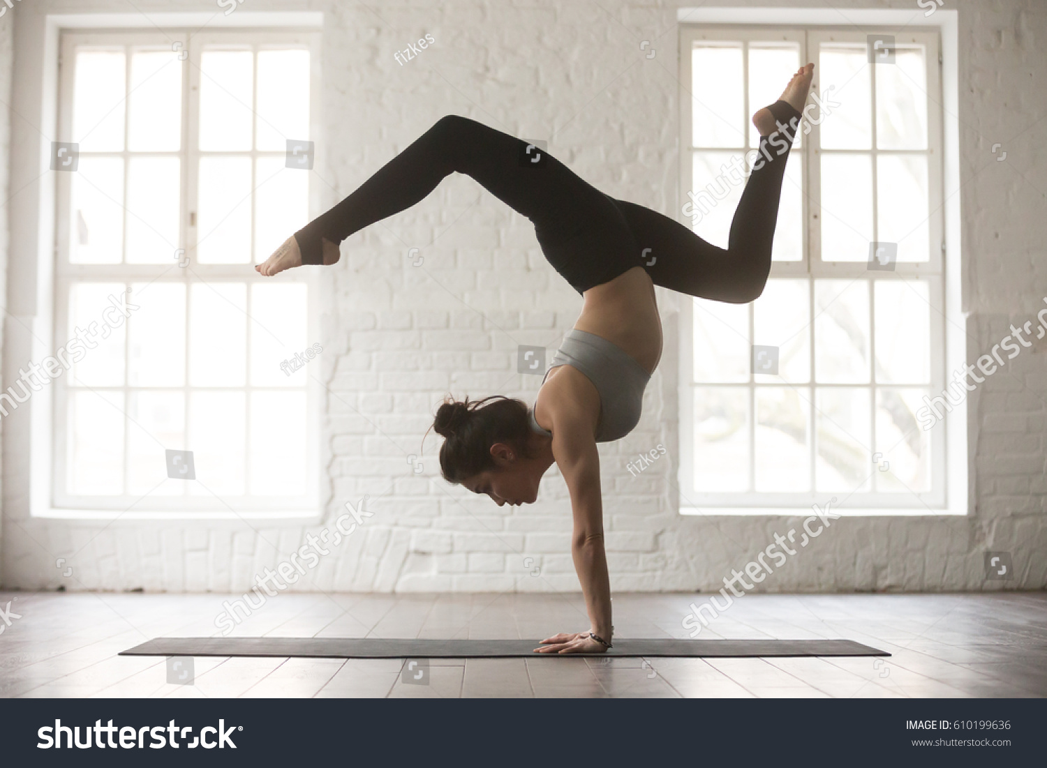 Silhouette of young cool attractive yogi woman practicing yoga concept, standing in Adho Mukha Vrksasana exercise, Downward facing Tree pose, working out, wearing sportswear bra and pants, full length #610199636