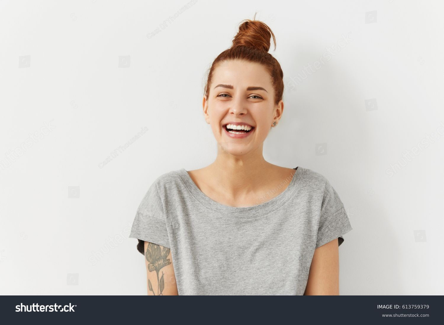 Happy cheerful young woman wearing her red hair in bun rejoicing at positive news or birthday gift, looking at camera with joyful and charming smile. Ginger student girl relaxing indoors after college #613759379