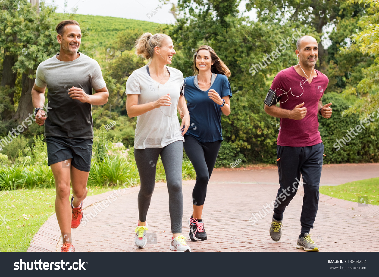Healthy group of people jogging on track in park. Happy couple enjoying friend time at jogging park while running. Mature friends running together outdoor. #613868252