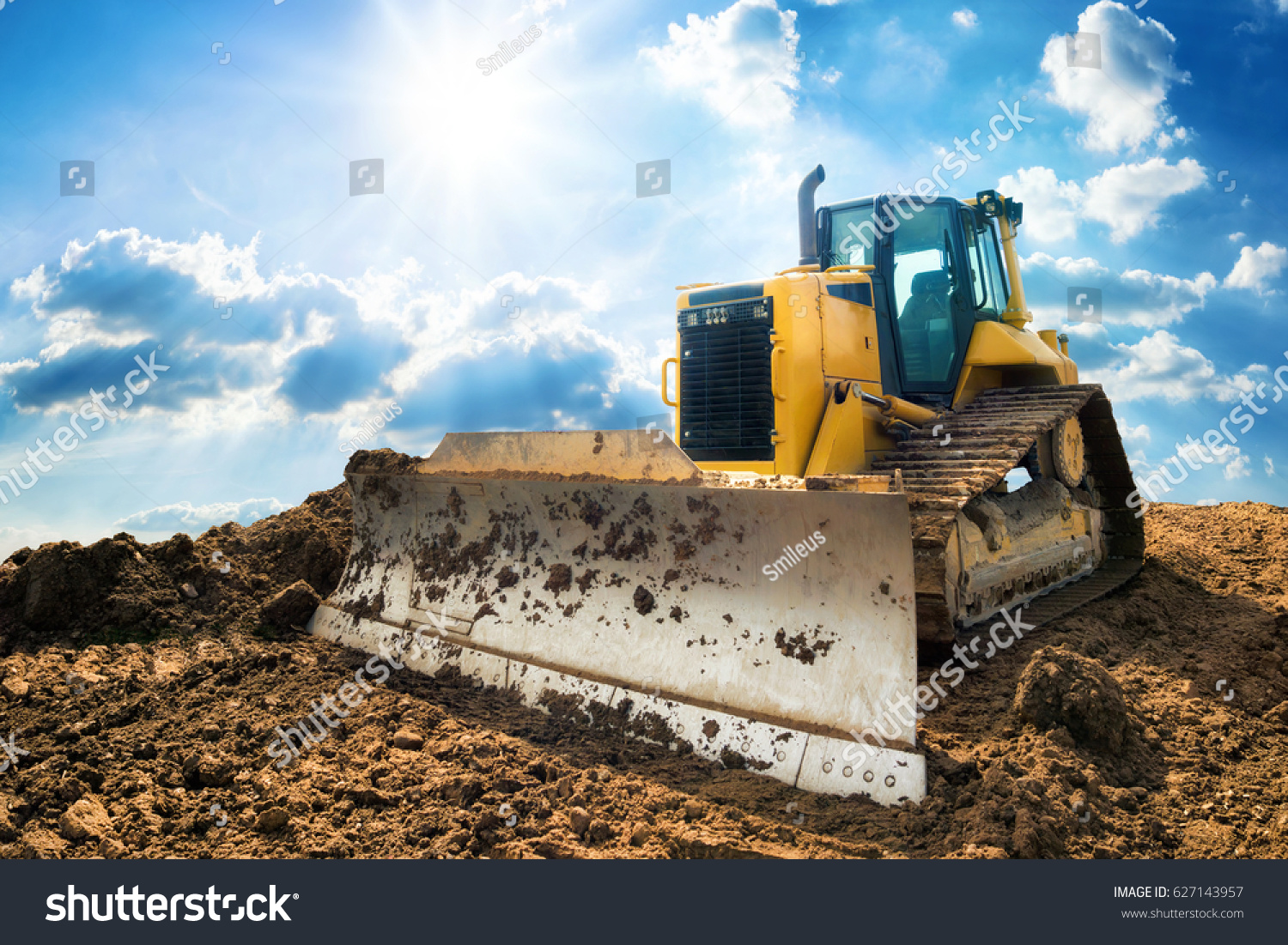 Yellow excavator on new construction site, with the bright sun and nice blue sky in the background #627143957