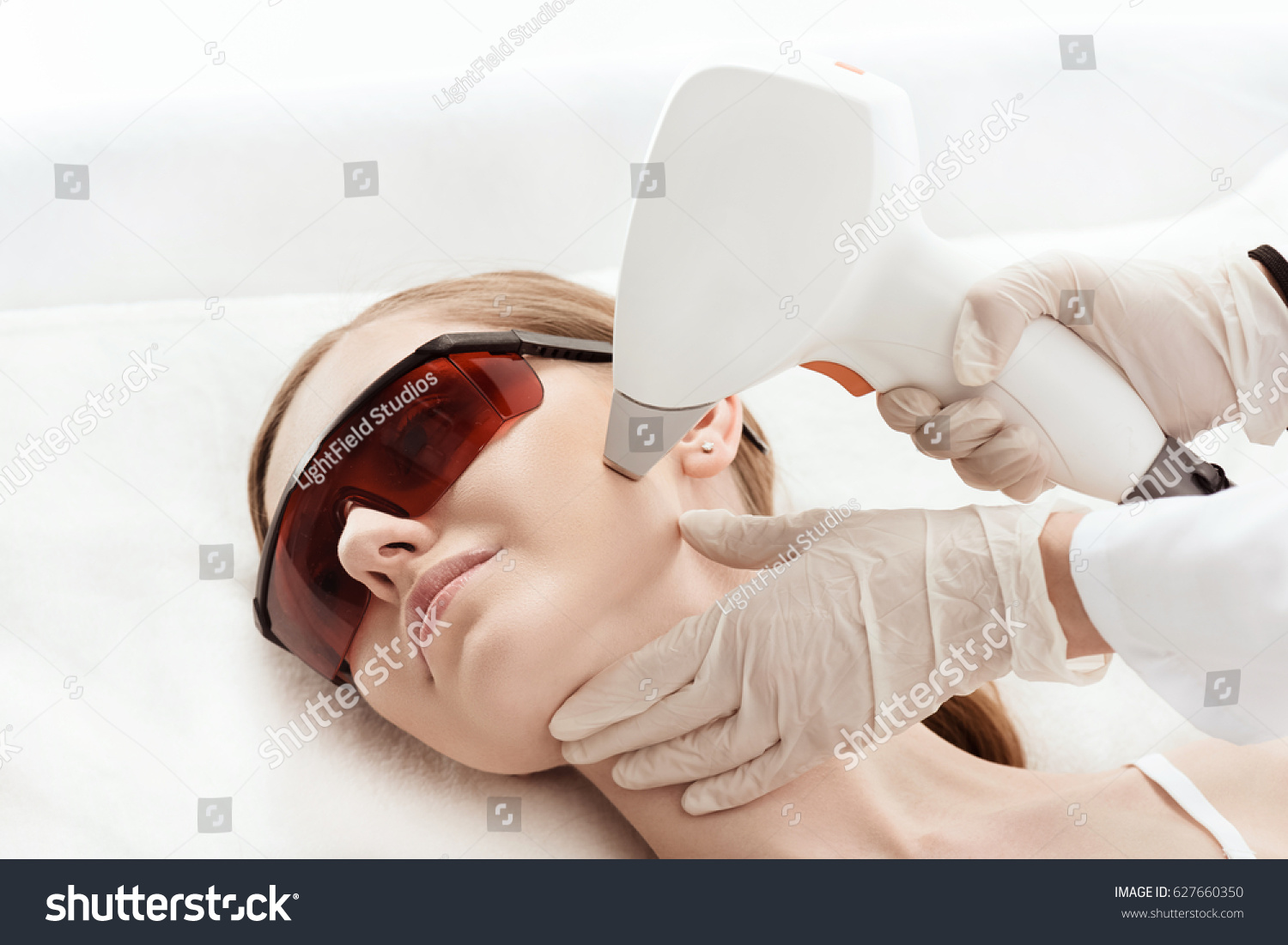Close-up view of young woman in uv protective glasses receiving laser skin care on face #627660350