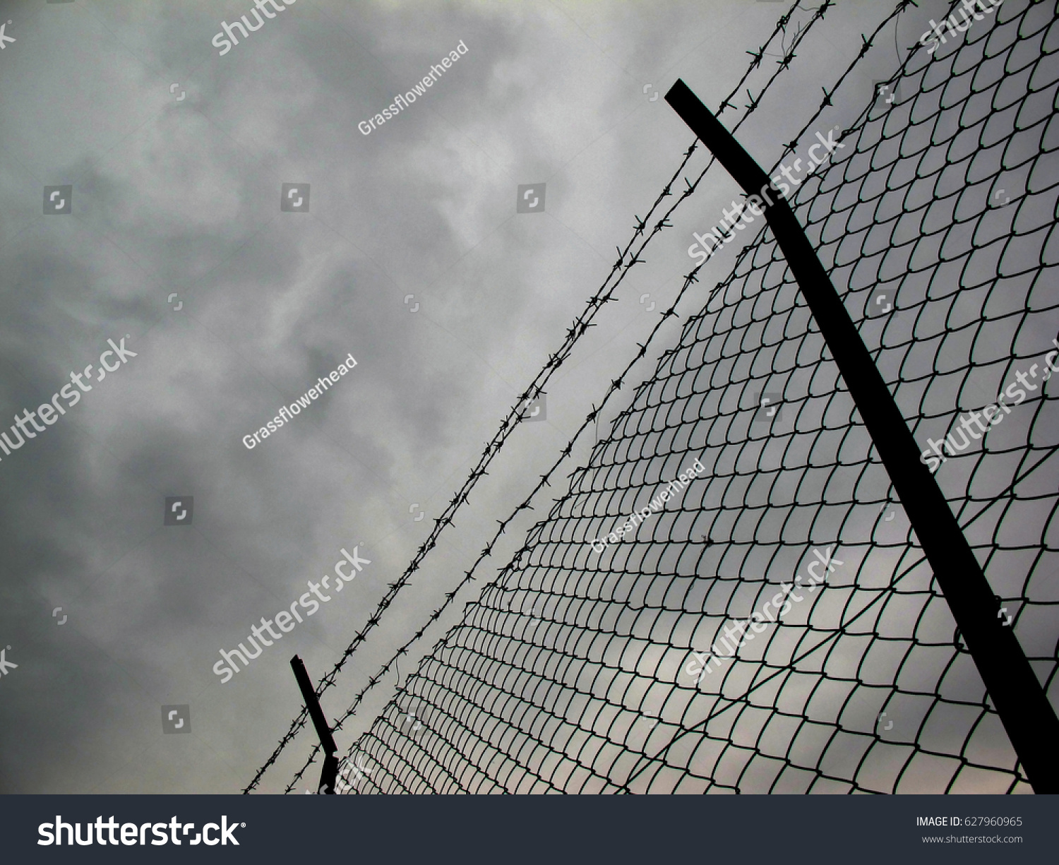 Low angle view of barbed wire and chain link fence against cloudy sky #627960965