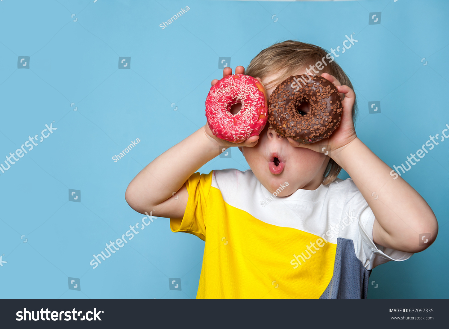 Little happy cute boy is eating donut on blue background wall. child is having fun with donut. Tasty food for kids. Funny time at home with sweet food. Bright kid. #632097335