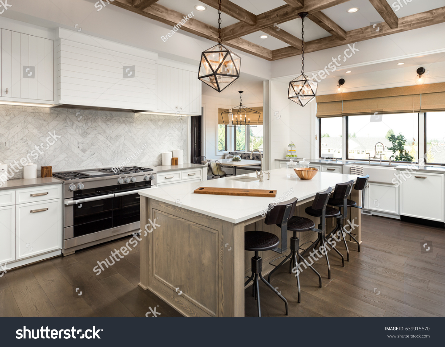 Kitchen Interior with Island, Sink, Cabinets, and Hardwood Floors in New Luxury Home. Features Elegant Pendant Light Fixtures, and Farmhouse Sink next to Window #639915670