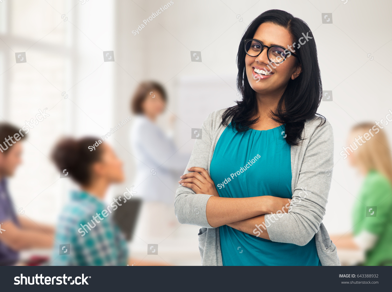 education, high school and people concept - happy smiling young indian woman or teacher in glasses over classroom background #643388932