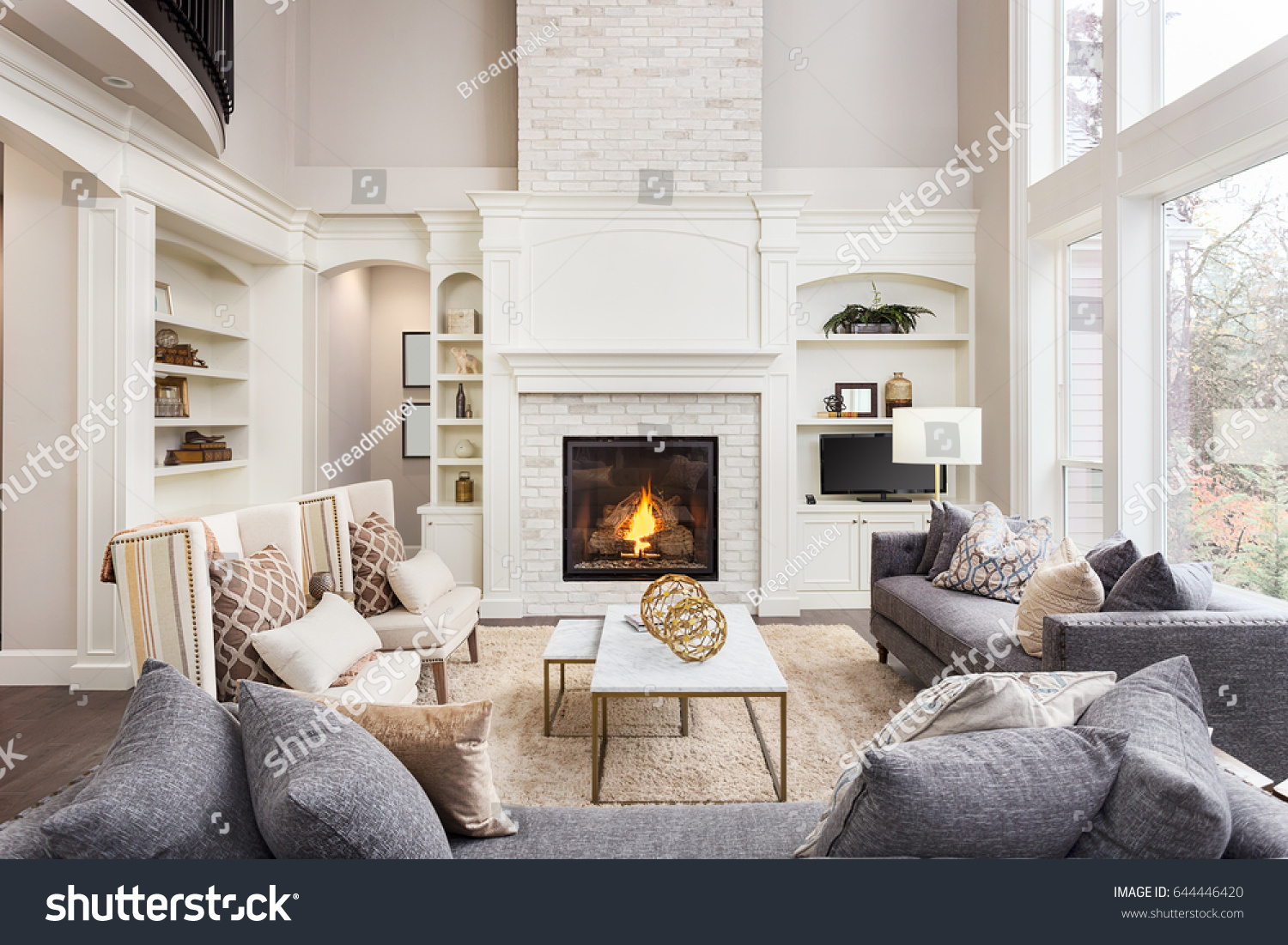 Beautiful living room interior with hardwood floors and fireplace in new luxury home. Large bank of windows hints at exterior view #644446420