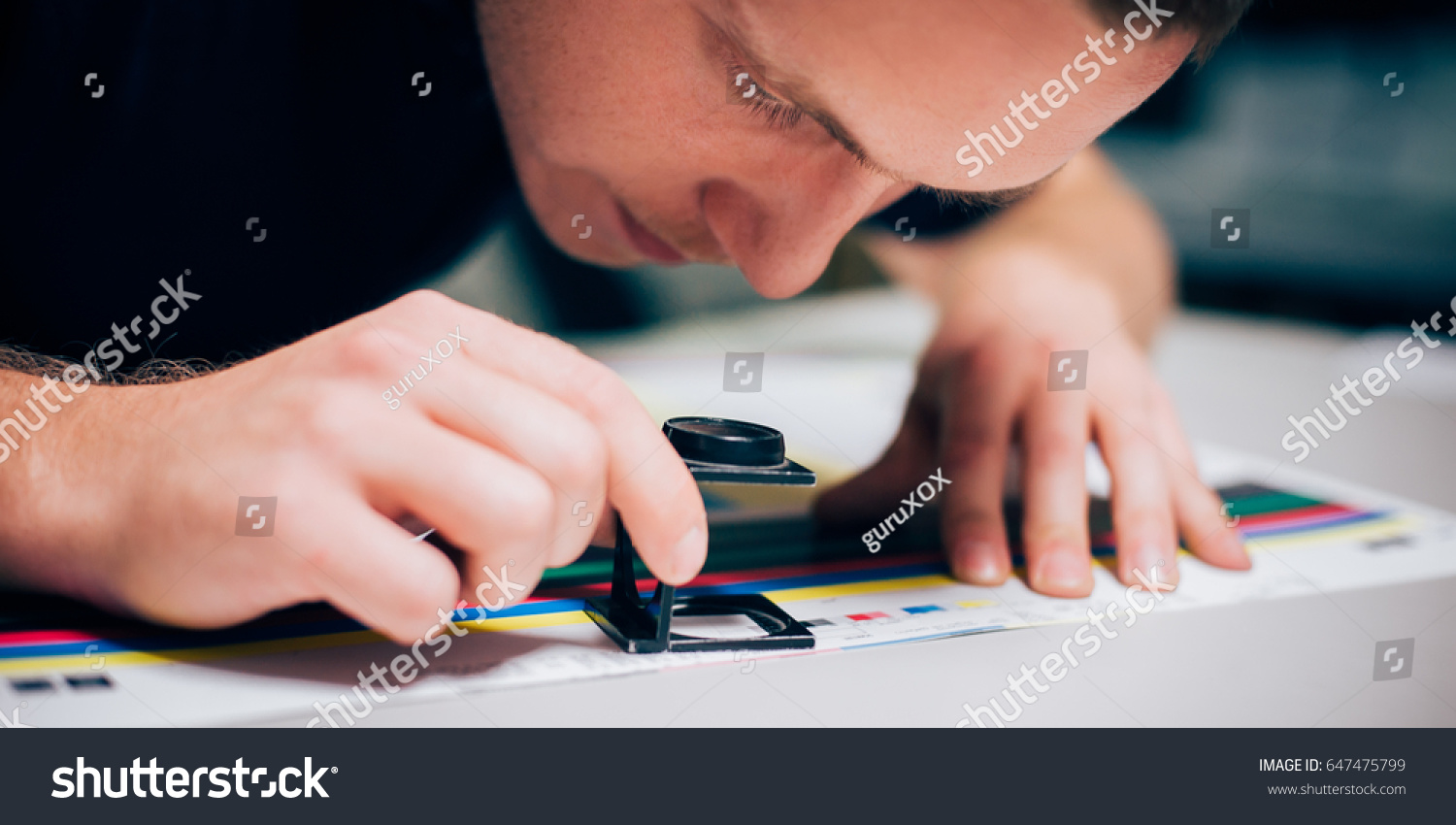 Worker in a printing and press centar uses a magnifying glass and check the print quality #647475799