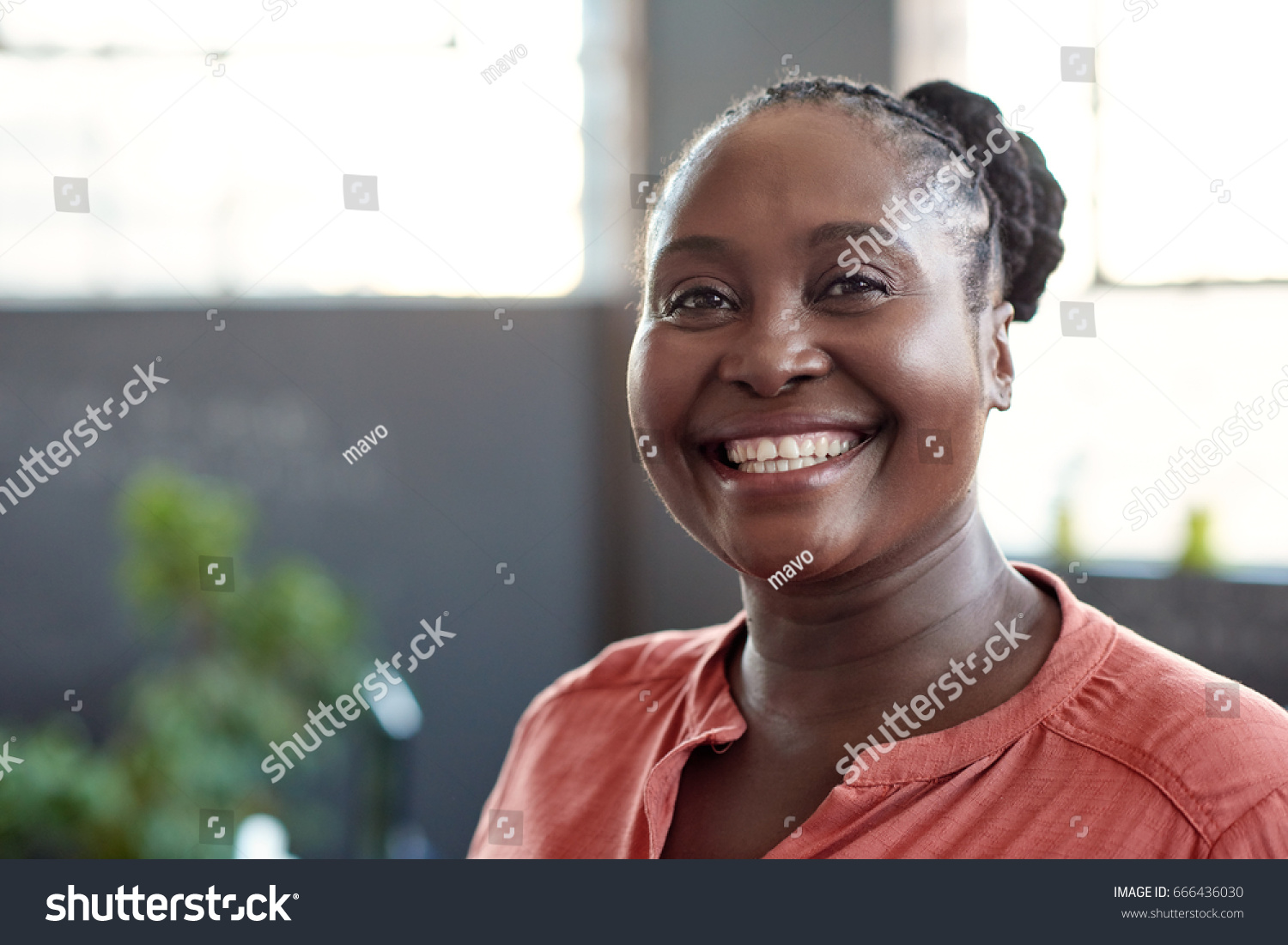 Portrait of a casually dressed young African businesswoman smiling confidently while standing alone in a bright modern office #666436030