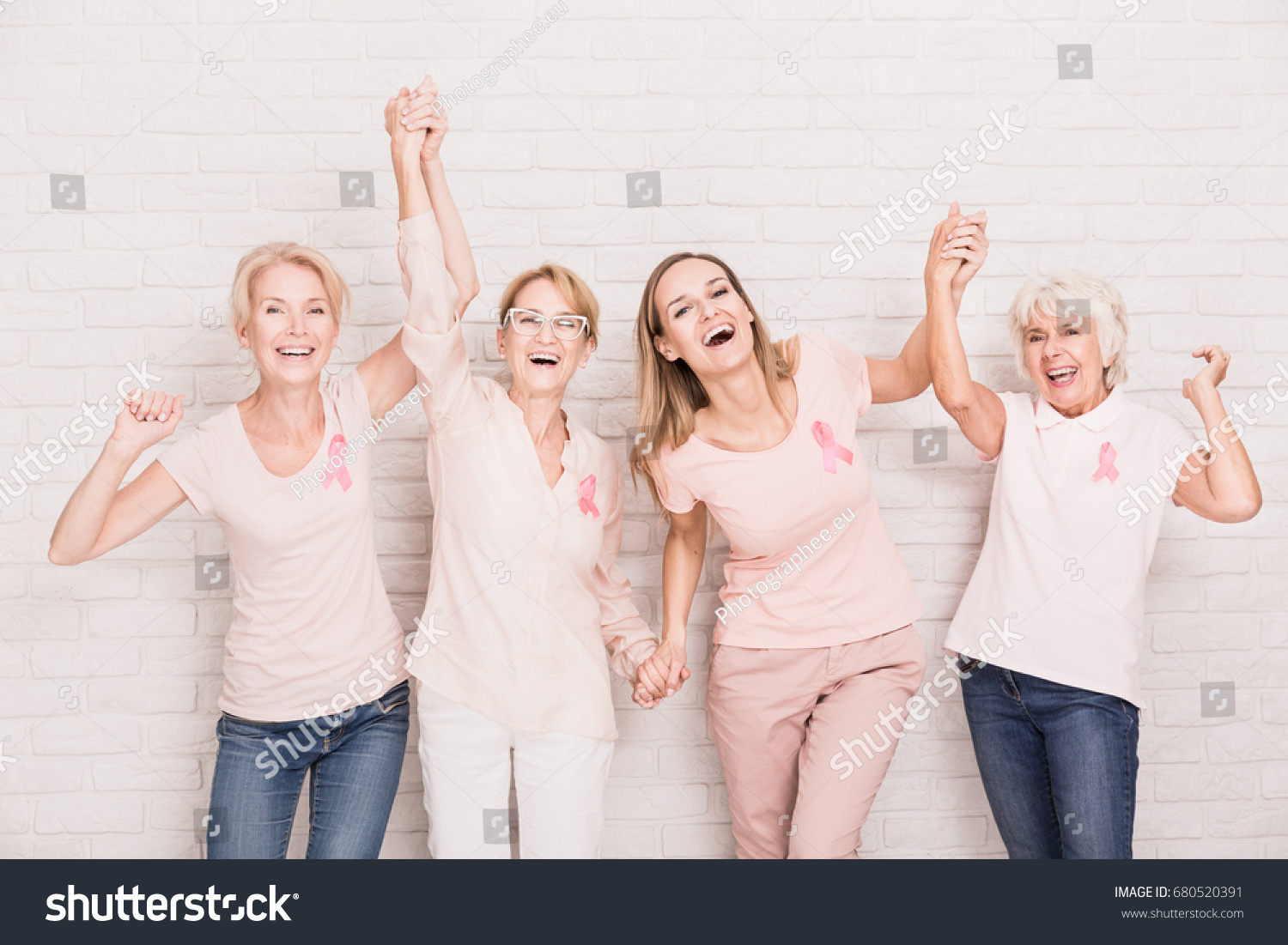 Group of smiling ladies with pink ribbons cheering and holding hands #680520391