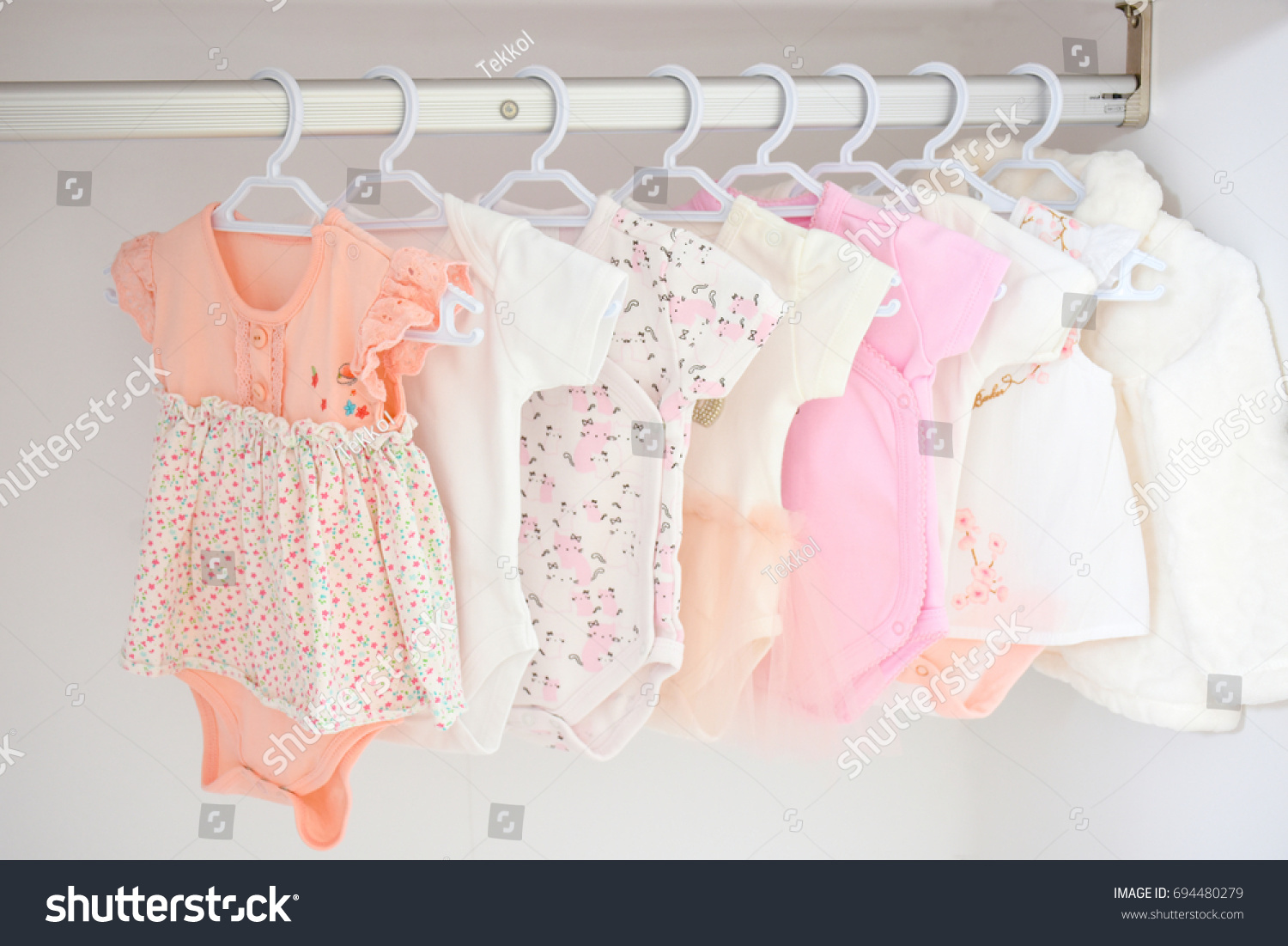 Colorful, cute girl baby dresses hanging on rack in wardrobe. Baby fashion concept design. #694480279